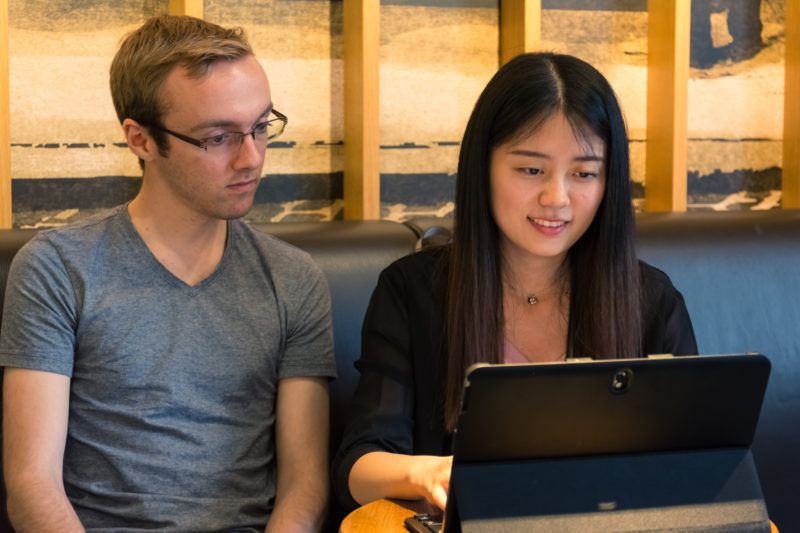 European Male and Asian Girl Working Togther on Laptop Tablet Co Ung mand og kvinde taler ved en bærbar computer.